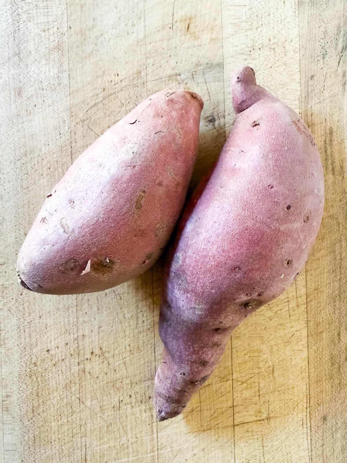 two sweet potatoes on a cutting board